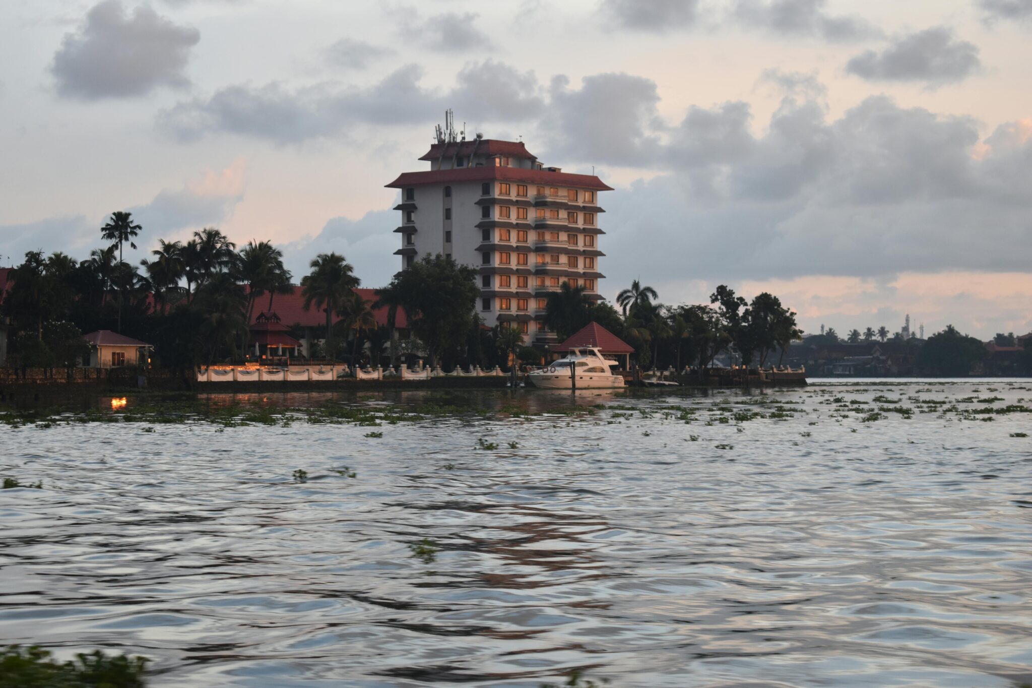Serene riverside scene featuring a multi-story hotel and palm trees at sunset.